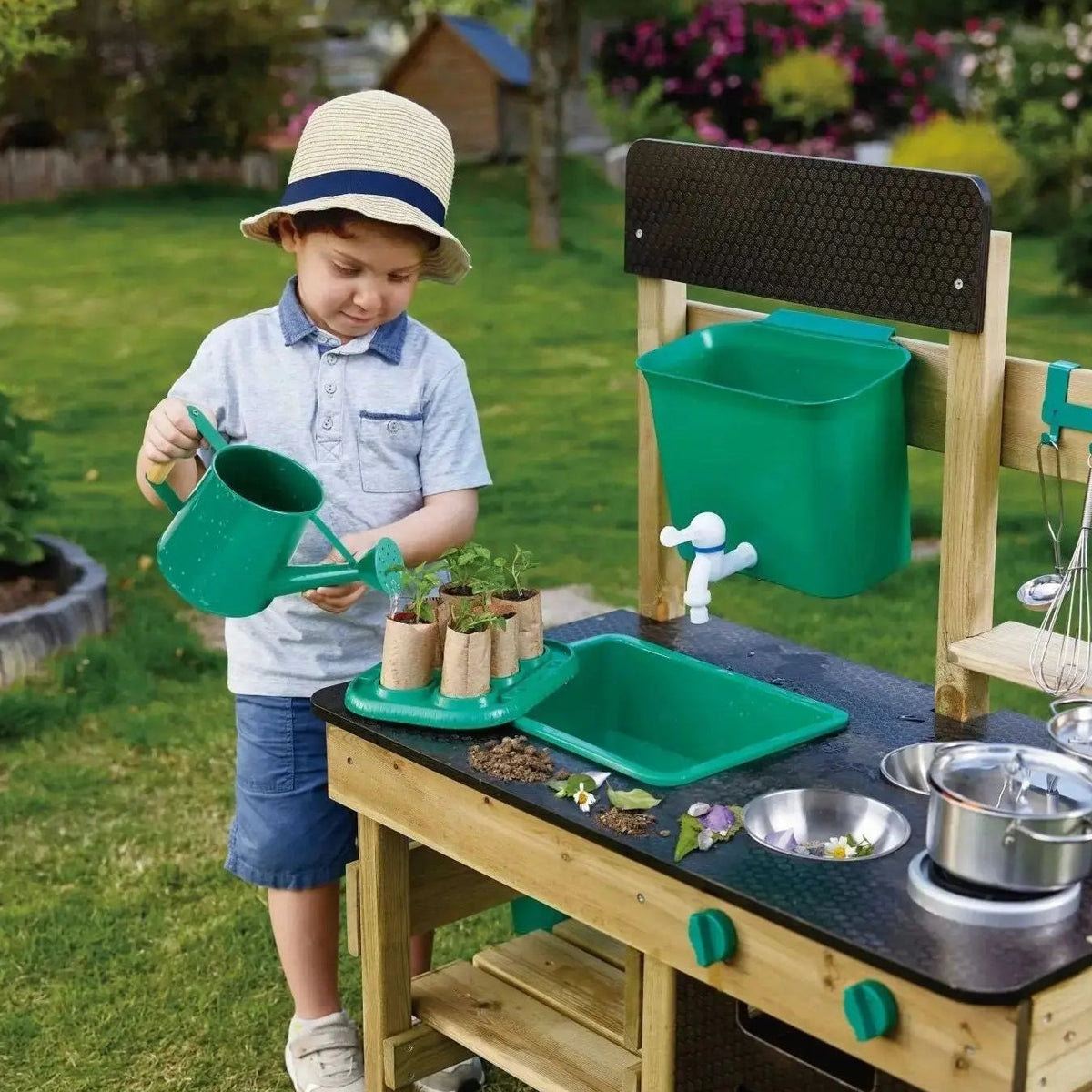 Child watering plants beside the Hape wooden outdoor mud kitchen with refillable water tank and sink