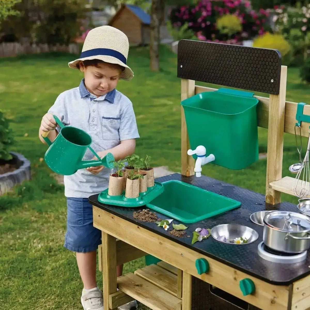 Child watering plants beside the Hape wooden outdoor mud kitchen with refillable water tank and sink